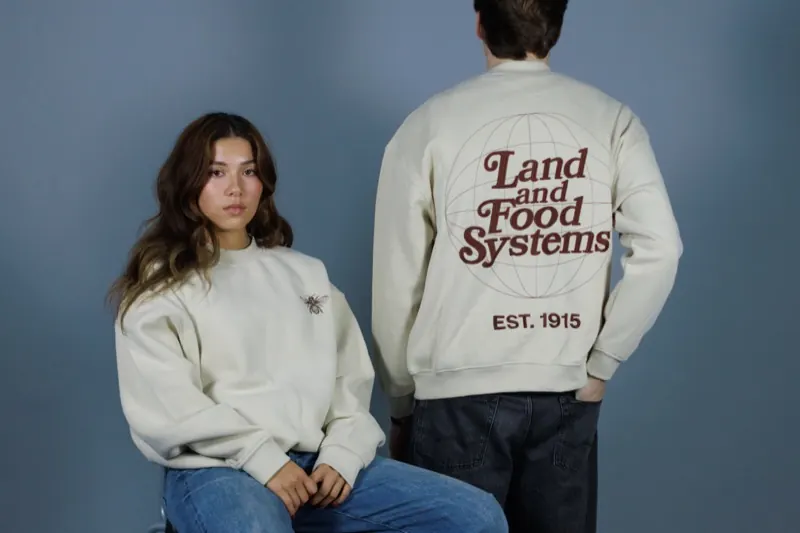 Two models in cream crewnecks; one shows the embroidered 'Land and Food Systems' back